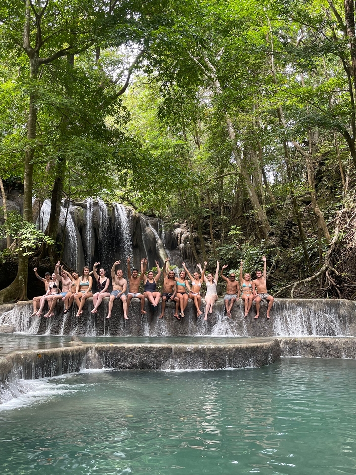 Group of people sitting in front of a waterfall, raising their hands.