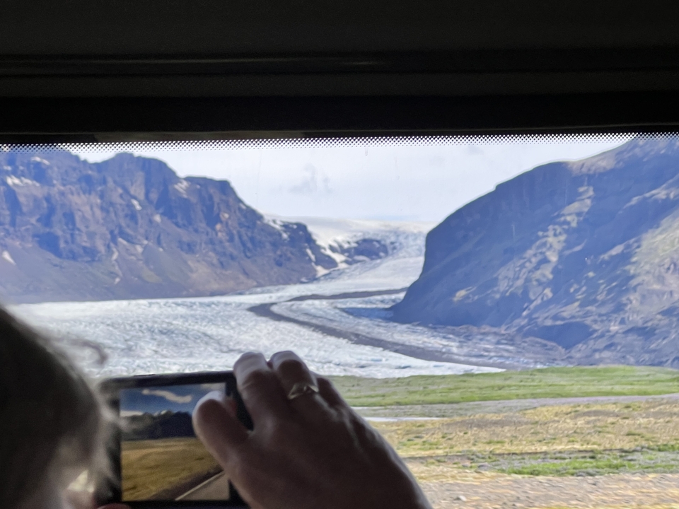 Person taking a photo of a glacier from a vehicle.