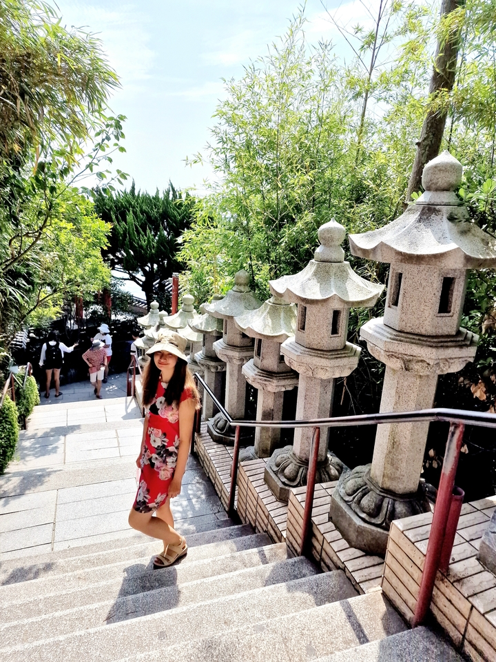Woman walking down steps lined with stone lanterns.