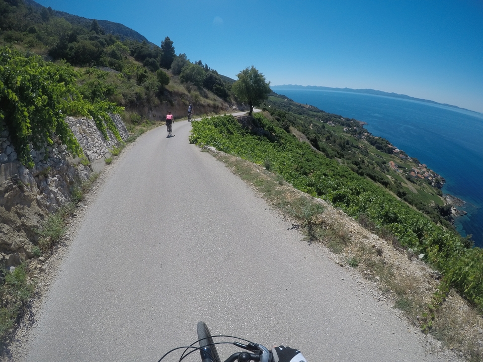 Cyclists riding on a scenic road with sea views and rolling hills.