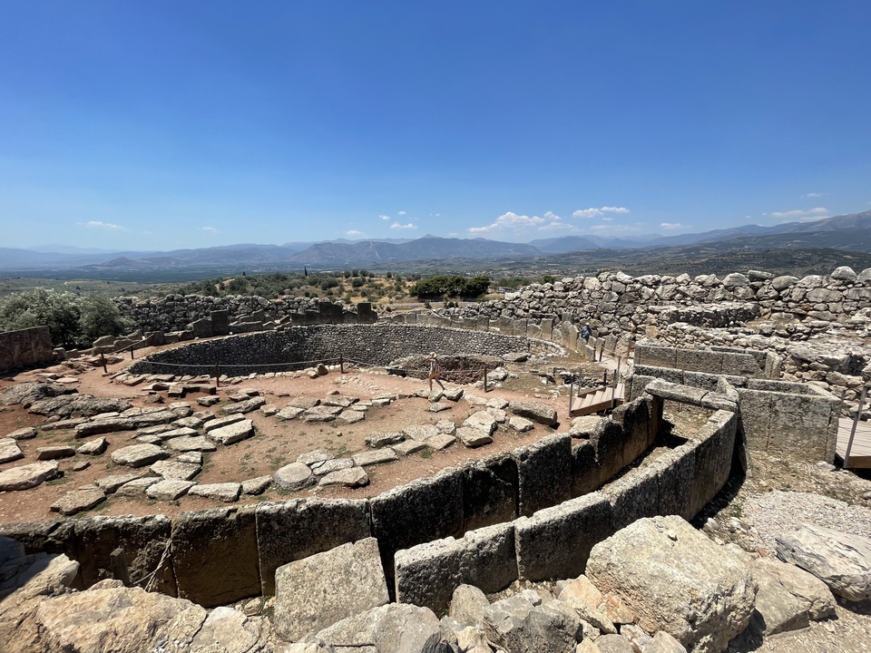 Ruines d'un site antique avec des murs de pierre et un arrière-plan montagneux.