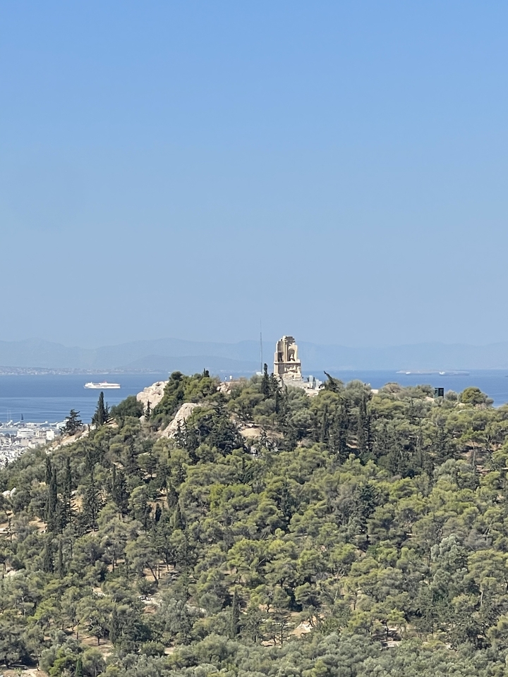 Monument au sommet d'une colline sur fond de mer avec un navire de croisière au loin.