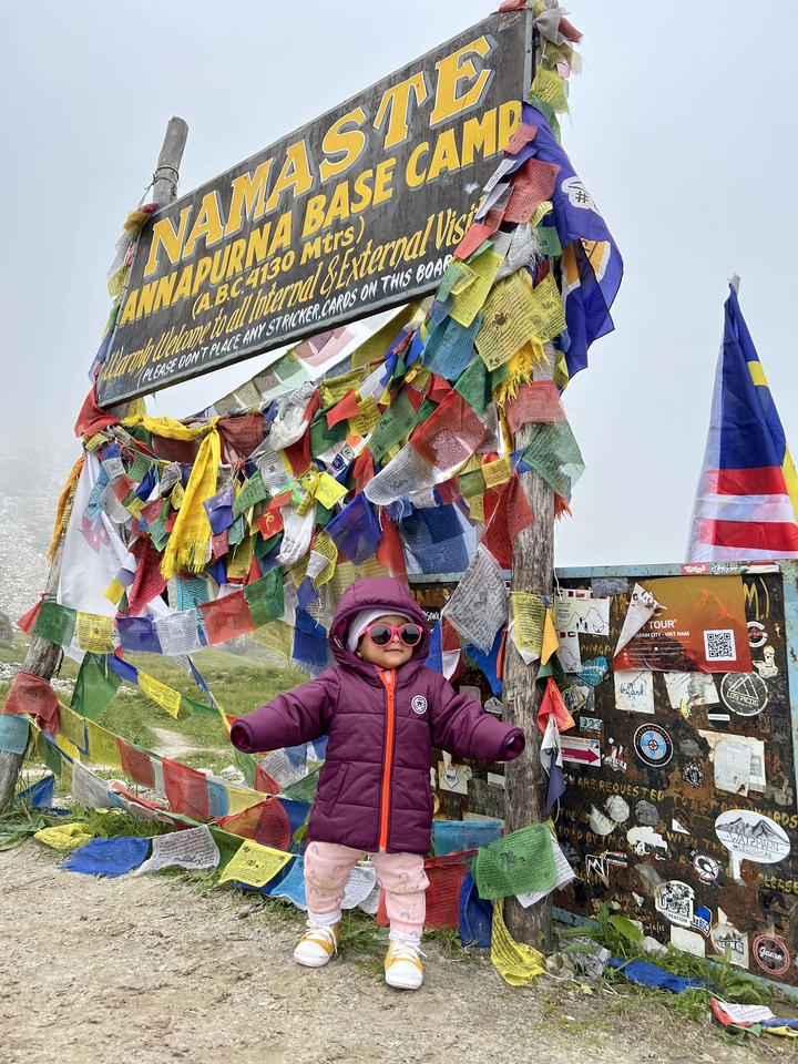 Un enfant portant des lunettes de soleil se tient parmi des drapeaux de prière colorés au camp de base de l'Annapurna.