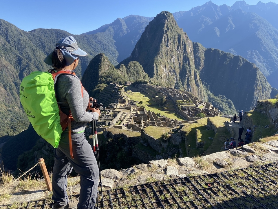 A hiker with a green backpack overlooks the Inca ruins at Machu Picchu.