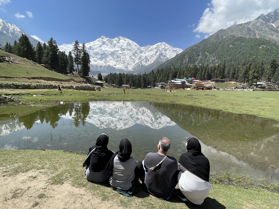 Group sitting by a reflective pond with snowy mountains in the background.