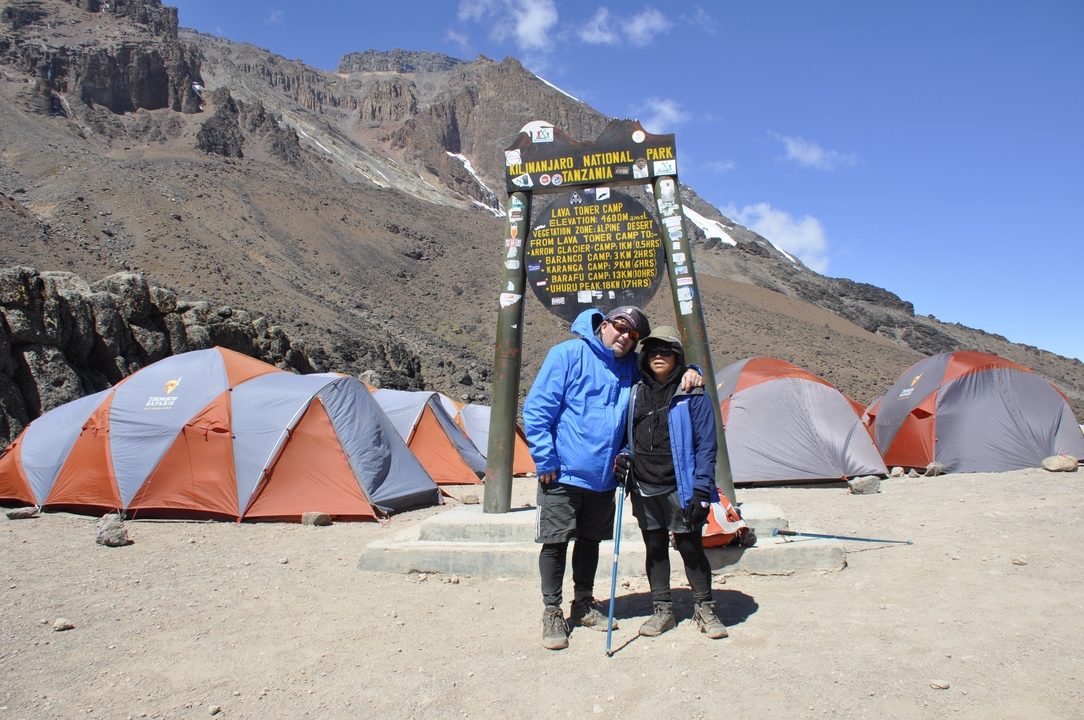 Two hikers posing by a Kilimanjaro National Park sign.