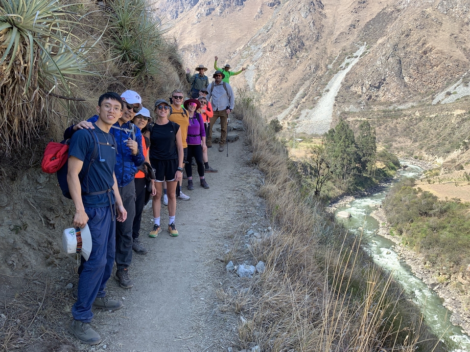 Group of hikers posing on a trail with river and mountains.