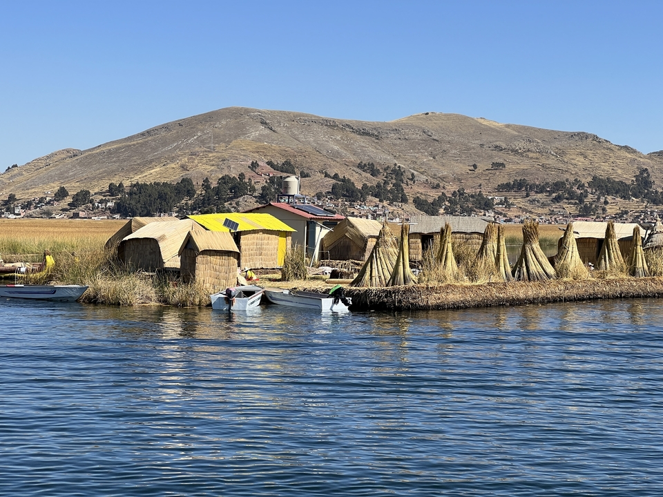 Floating reed islands with thatched huts and hills in the background.