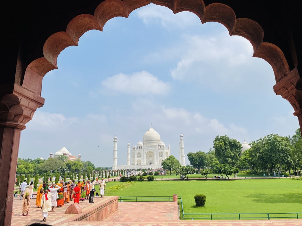 The Taj Mahal in the distance framed by an arch with people in the foreground.