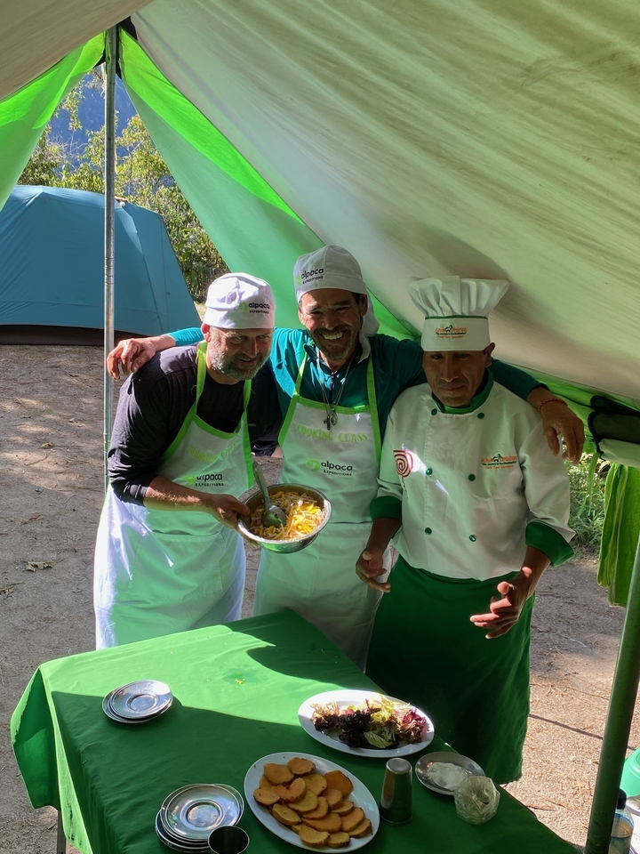 Two chefs with a tourist, holding a dish in a campsite.