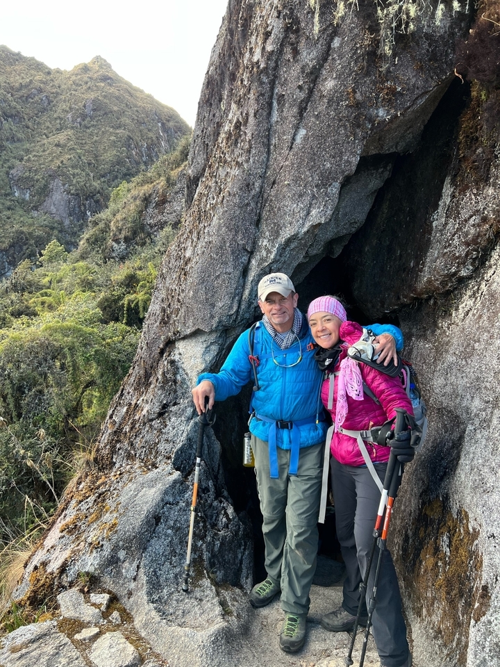 A couple posing in hiking attire in front of a rocky cave.