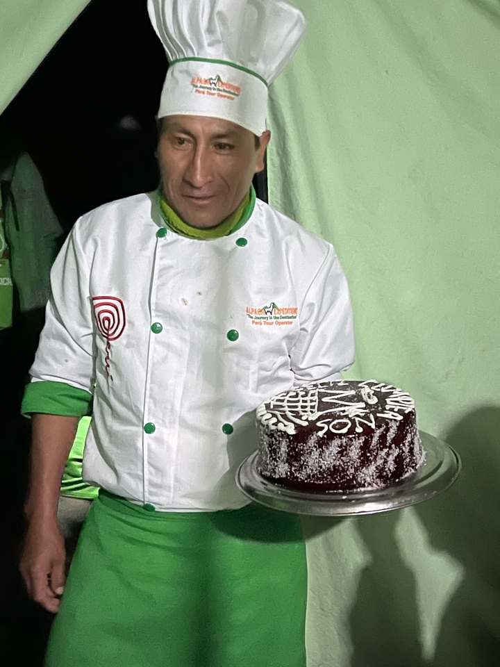 A chef presenting a decorated cake at a campsite.