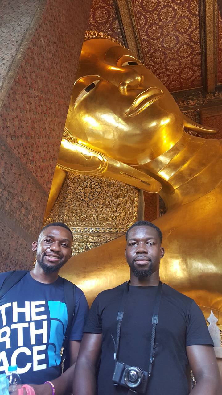 Two people posing in front of a golden reclining Buddha statue.