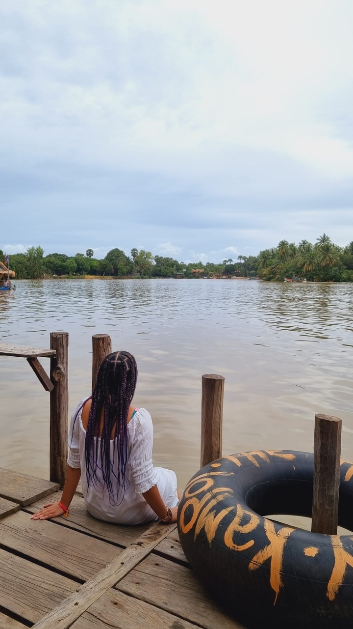 Person sitting on a wooden dock overlooking a river or lake.