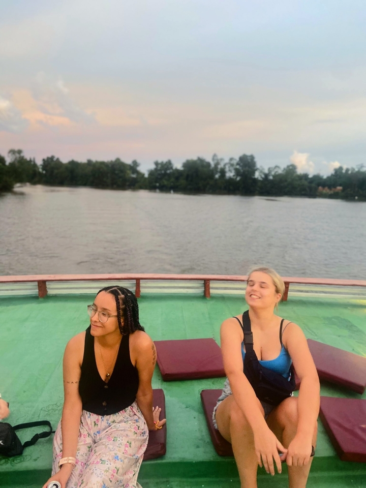 Two women on a boat, enjoying a sunset over a river.