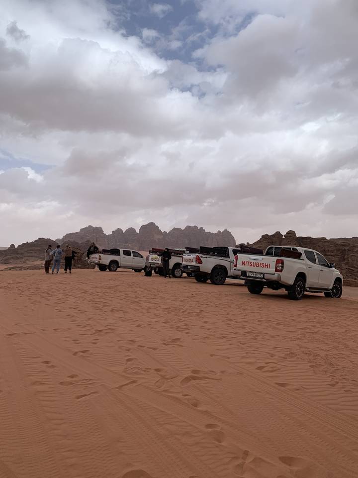 Vehicles parked on a desert landscape with cloudy sky.