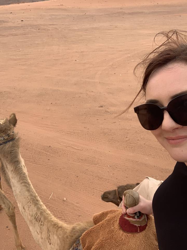 A person wearing sunglasses riding a camel in the desert.