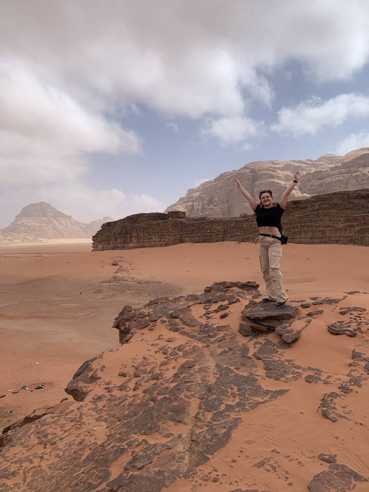 A person posing with arms raised in a desert landscape.