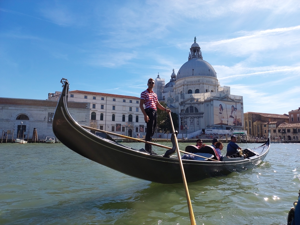 Gondolier rowing a gondola with a historic church in the background.