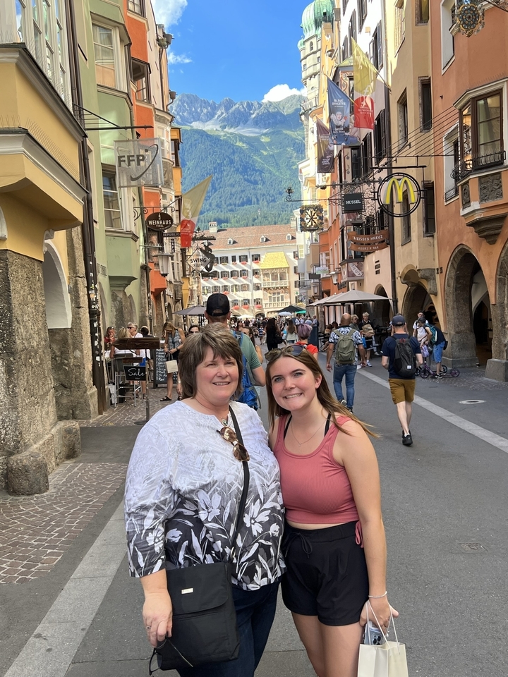 Two women posing on a quaint cobblestone street with historic buildings.