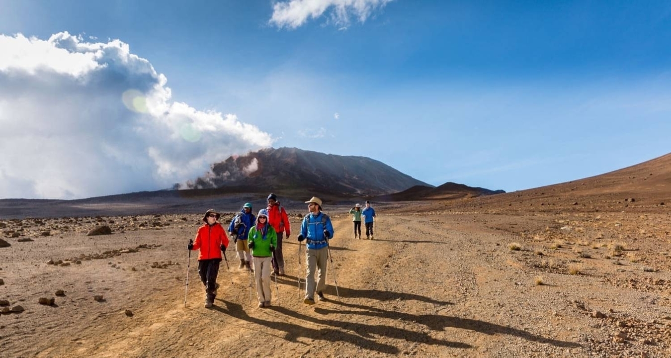Hikers on a barren, rocky landscape under a bright sky.