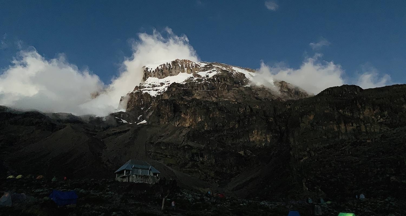 A mountain partially covered in clouds with tents at the base.