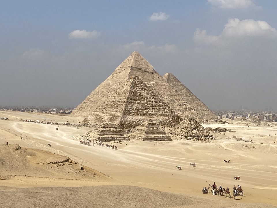 The pyramids of Giza with a few tourists in the distance and a clear sky.