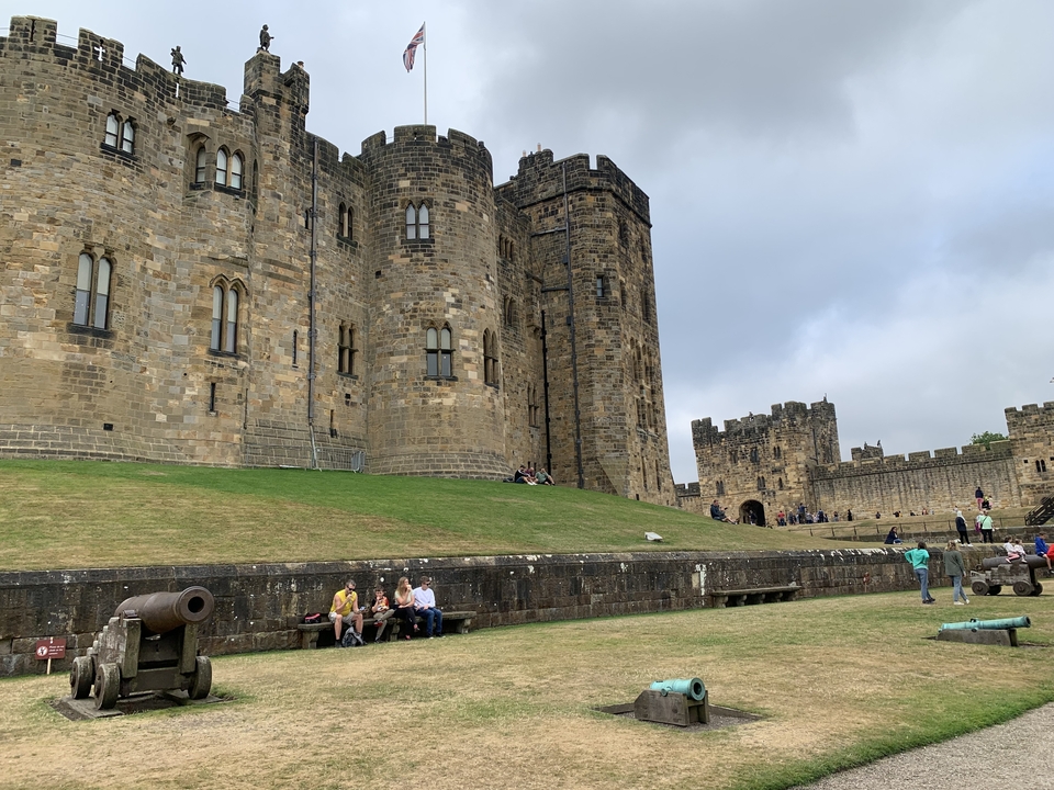 Visitors sitting by the walls of a large historical castle.