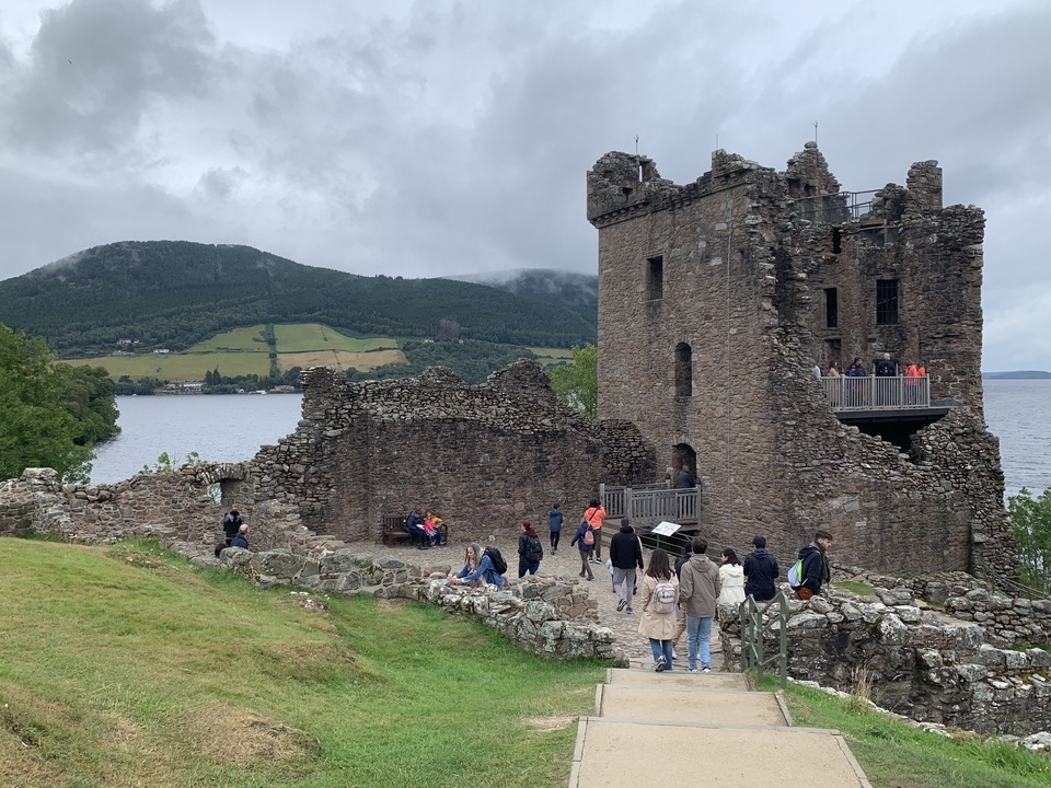 Historic castle ruins by a loch with tourists exploring the area.