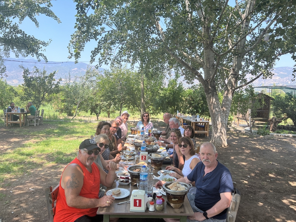 Group of people dining at a long outdoor table under trees.