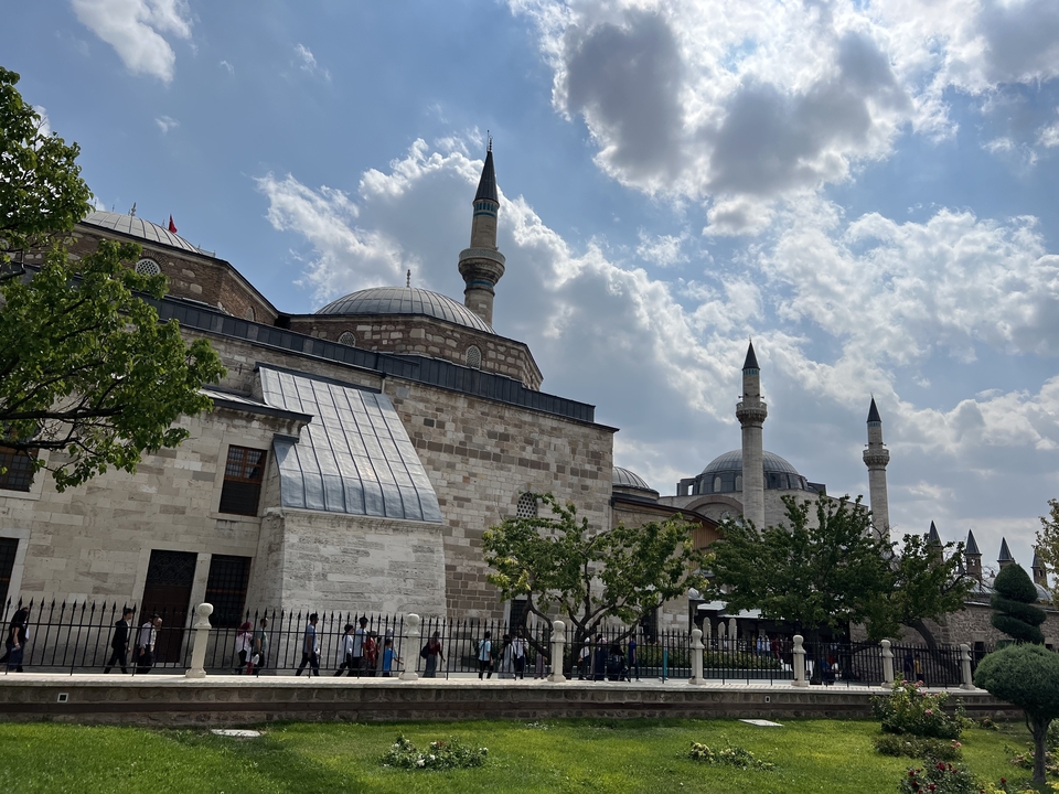 Large mosque with multiple domes and minarets, with people walking below.