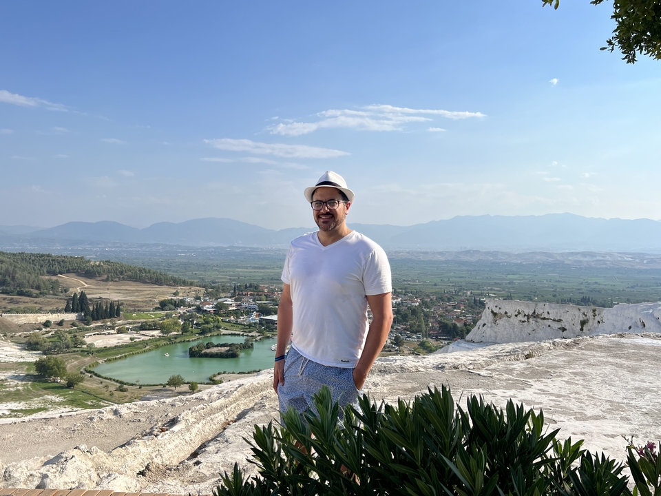 Person posing on a hill with a panoramic view of the landscape and a natural pool.