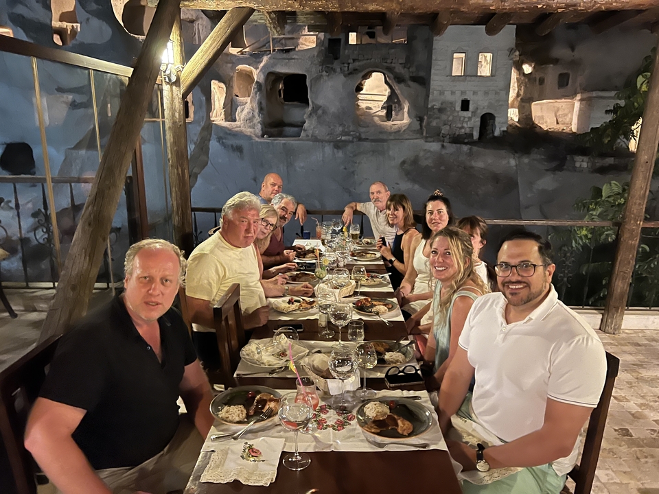 Group dining at a long table outside, with cave dwellings in the background.