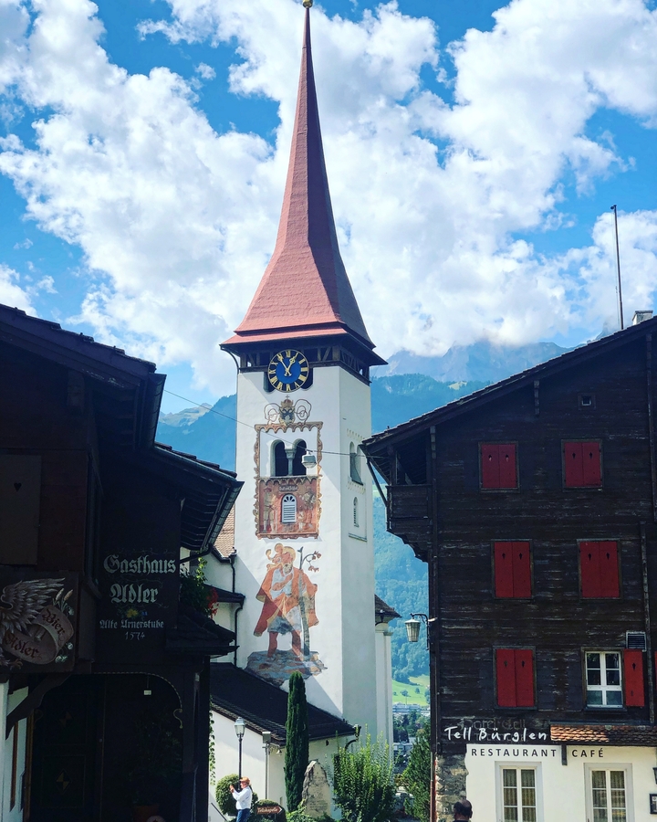 Church tower with clock, surrounded by mountainous backdrop.
