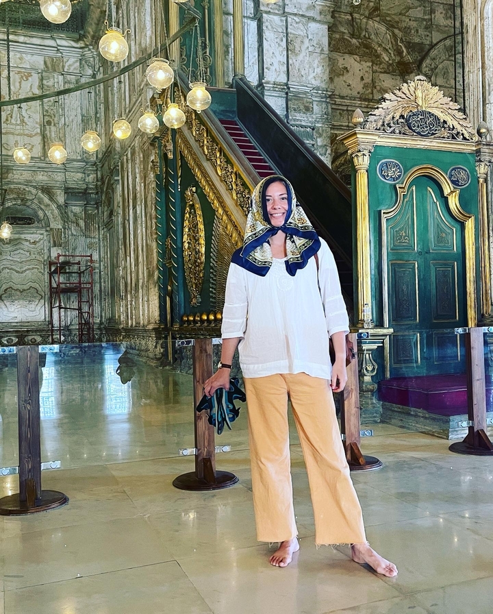 A woman standing inside an ornately decorated interior, possibly a mosque.
