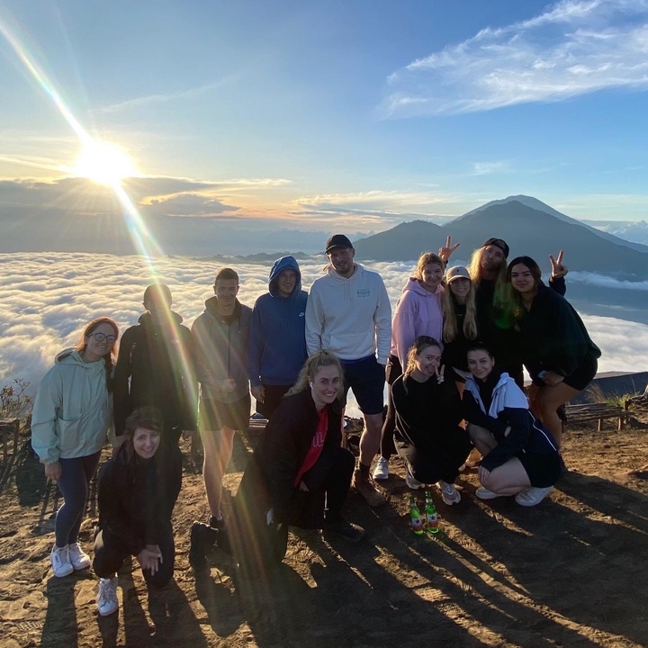 Groepsfoto op een bergtop met wolken eronder.