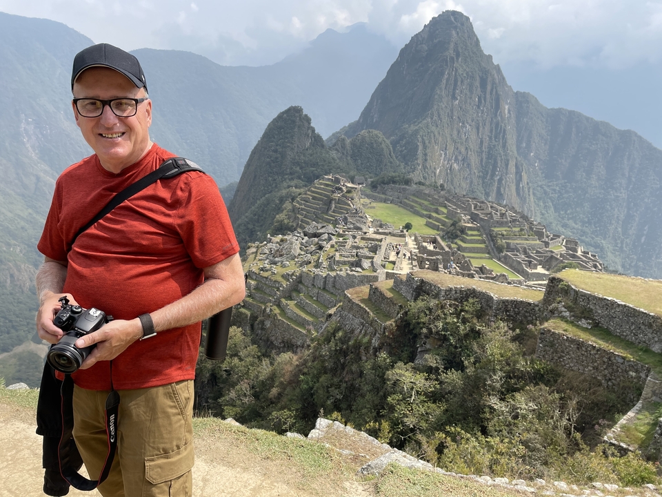 Homme avec appareil photo posant devant les ruines du Machu Picchu.