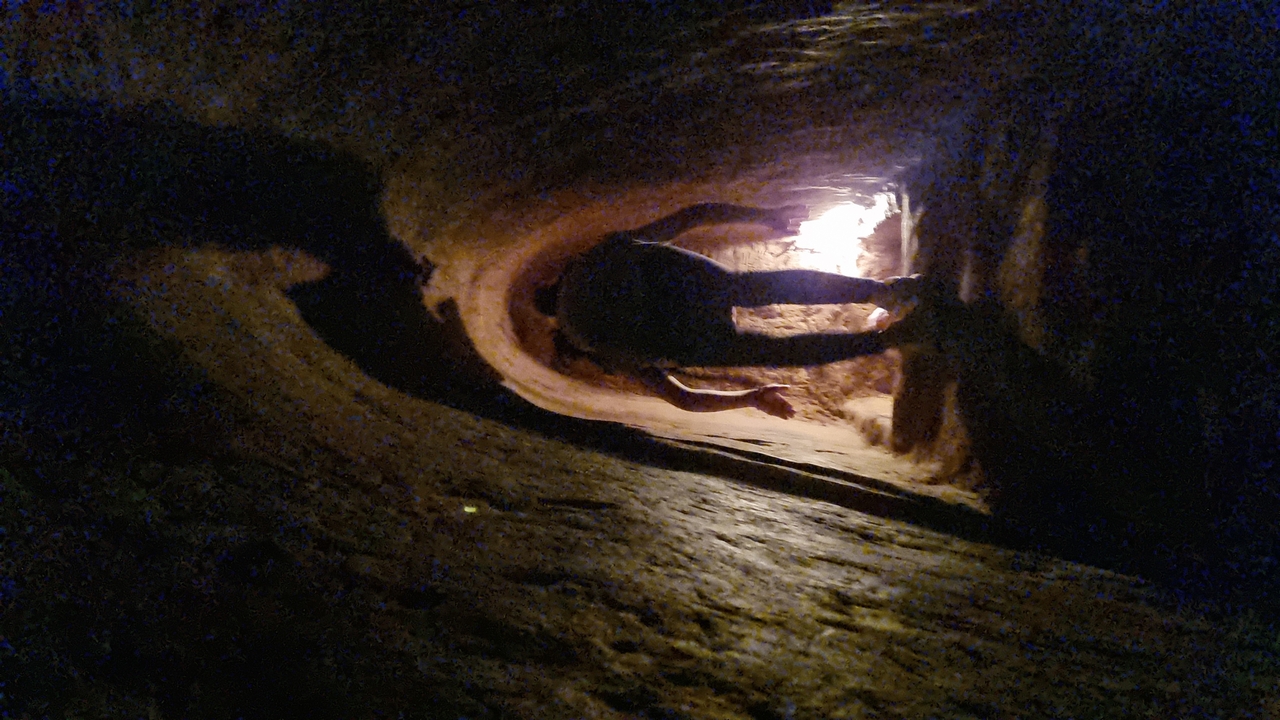 Person crawling through a narrow tunnel underground.