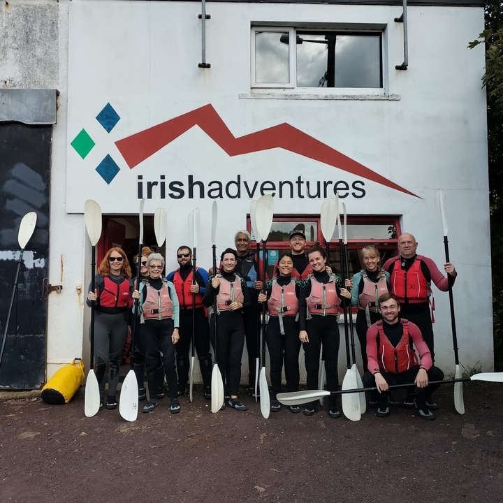 Group of people standing with kayaking gear in front of a building.