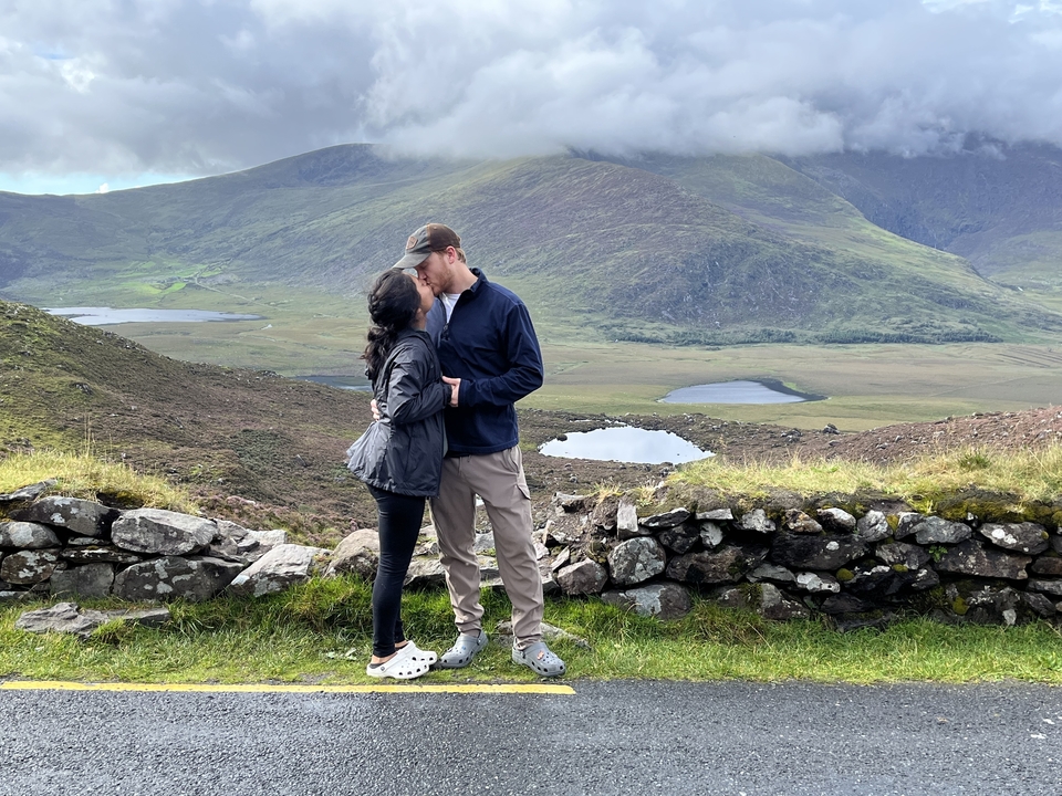 Couple kissing on a scenic hilltop with lakes in the background.