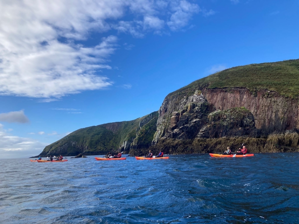 Group of people kayaking near steep cliffs.