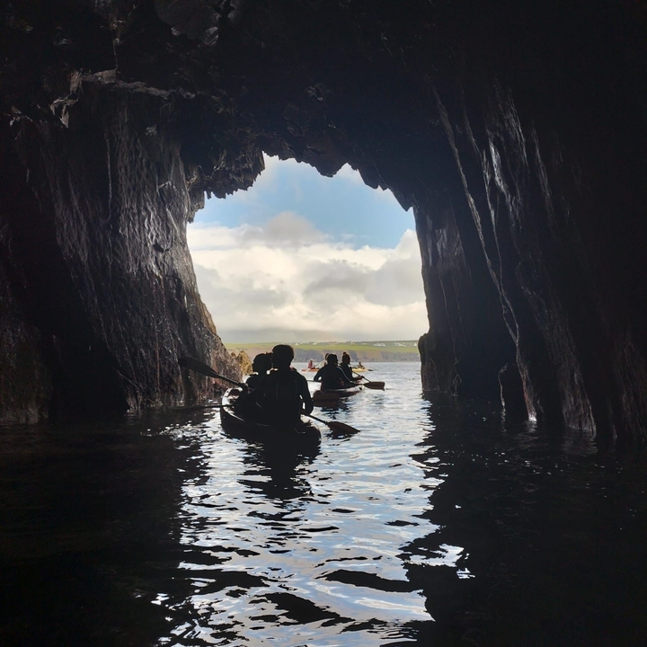 Kayakers in a dark cave with the sea visible beyond.