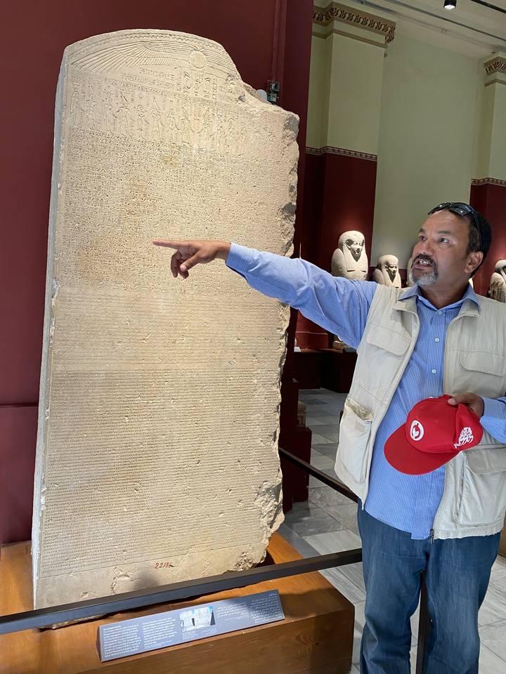 Visitor pointing at a large ancient stele with hieroglyphics.