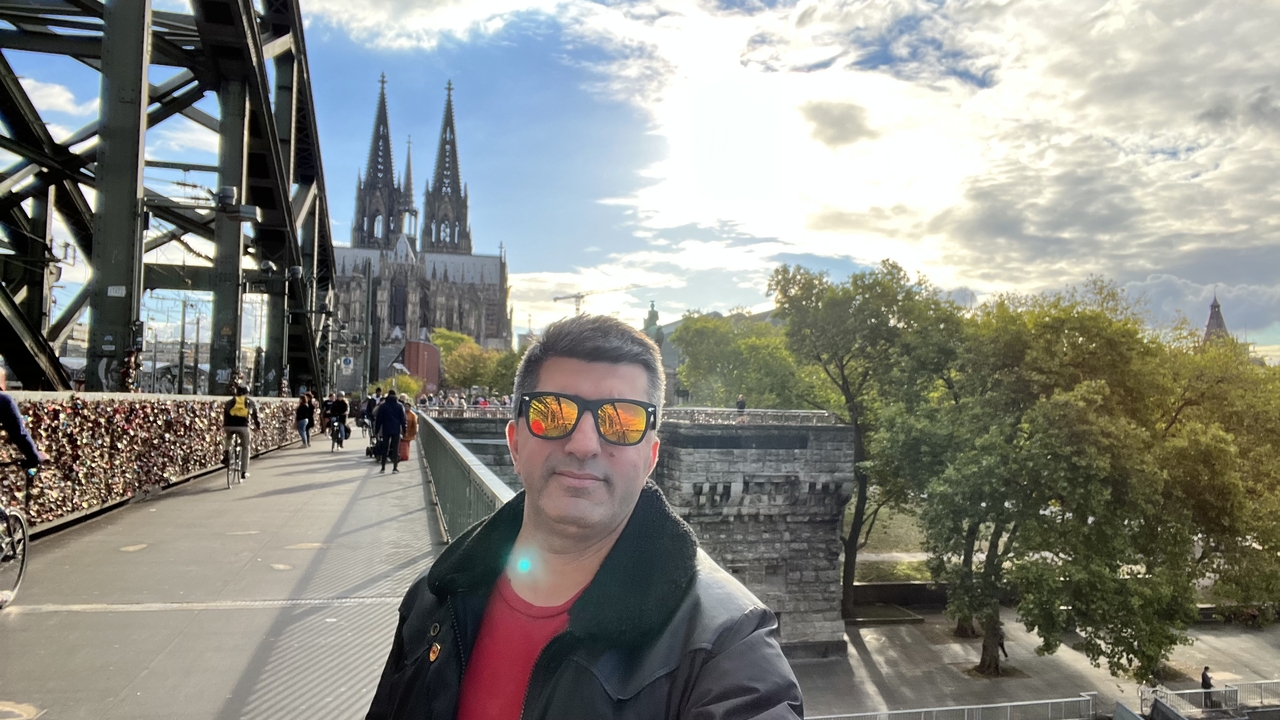 Homme posant près d'un pont avec une cathédrale en arrière-plan.