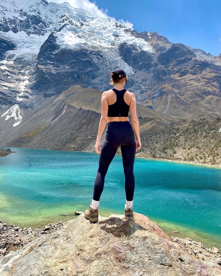 Femme debout près d'un lac alpin entouré de montagnes.