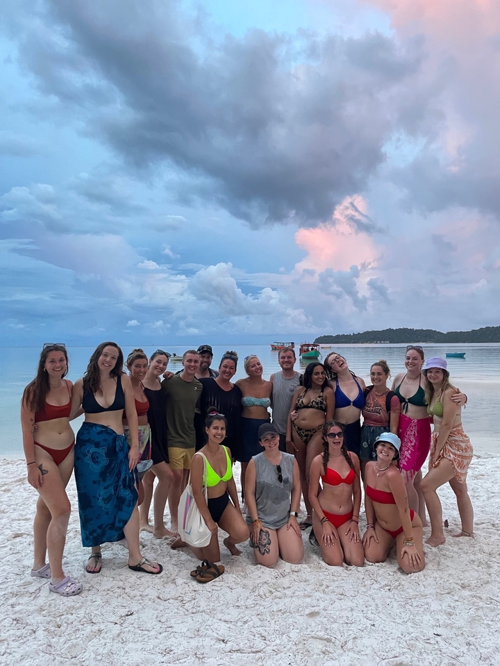 Group of people posing on the beach with boats in the background.