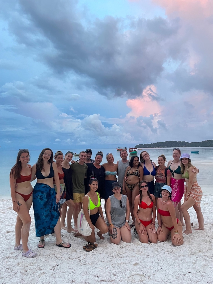 Group of people, some in swimwear, posing on the beach.