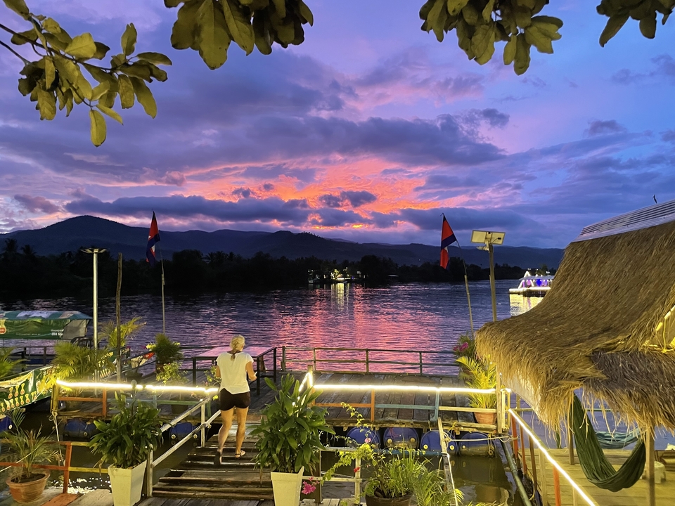 Person enjoying a view of a river under a vibrant sunset.