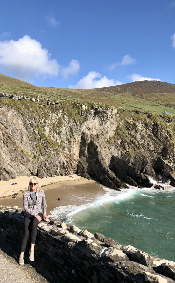Femme sur une plage avec des falaises rocheuses derrière.