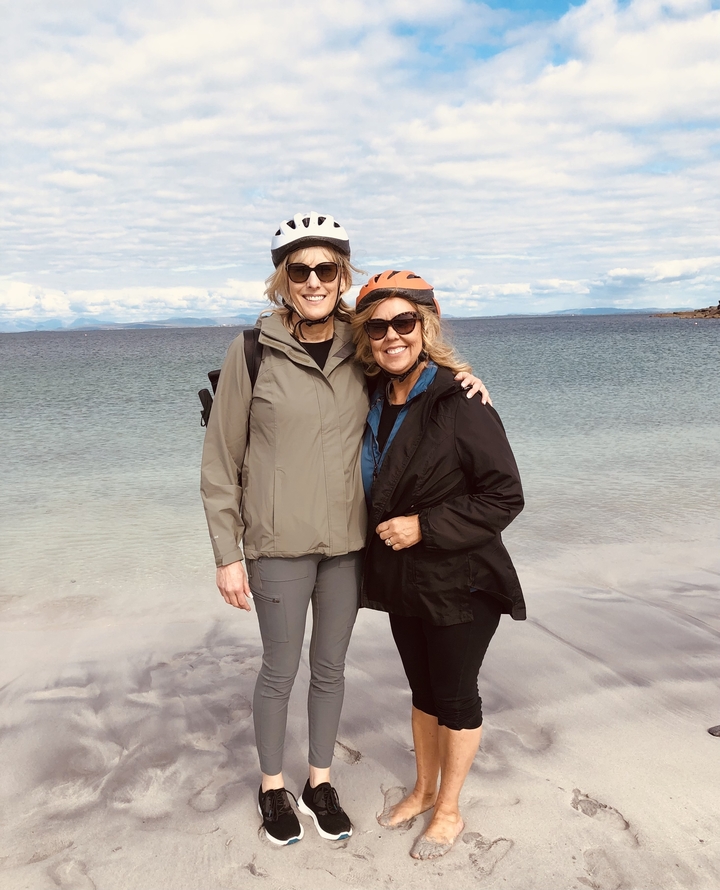 Two women posing on a beach with helmets.